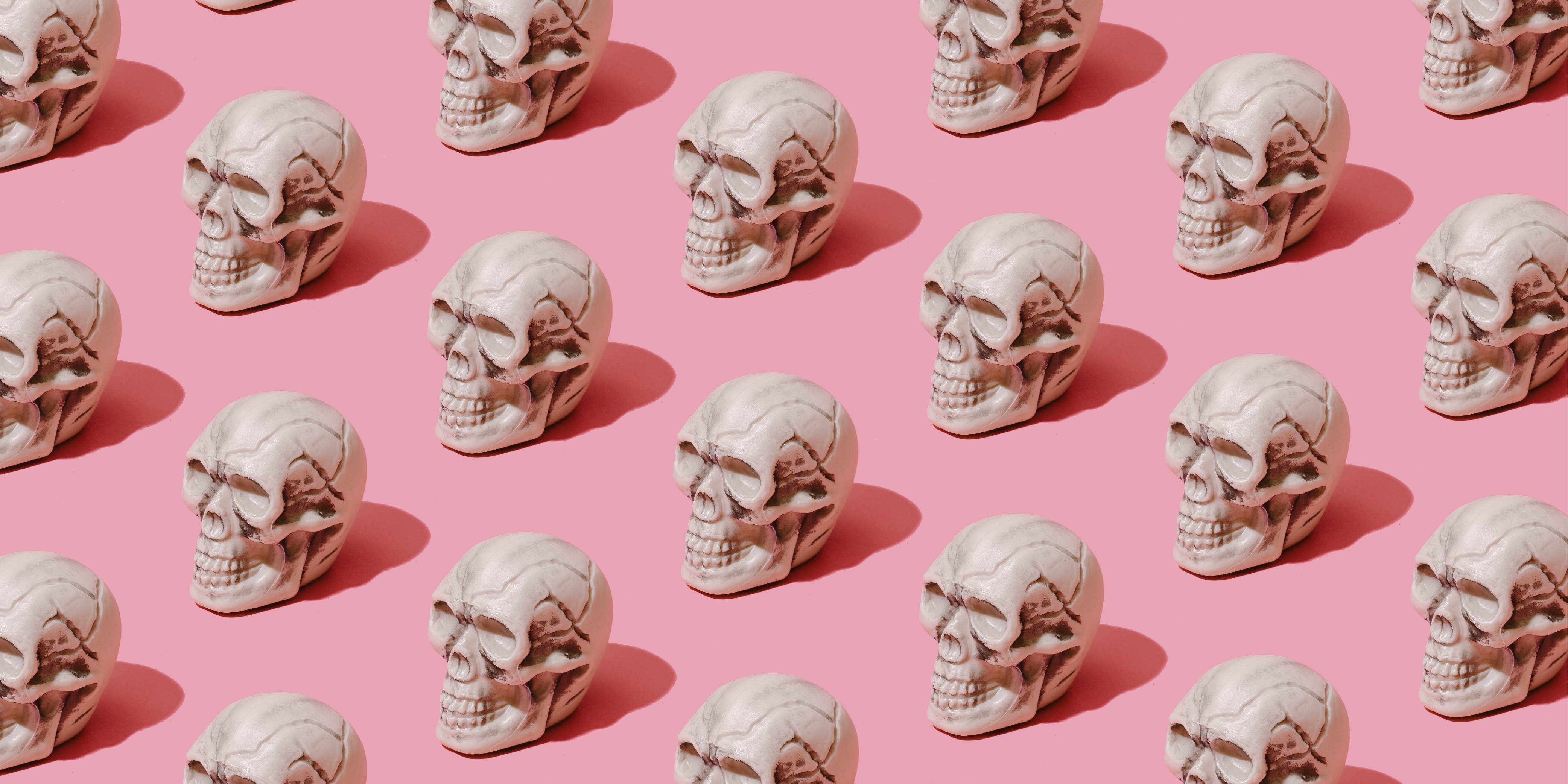 Abstract conceptual stock photo of small plastic skulls in a repeating pattern on a bright pink backdrop