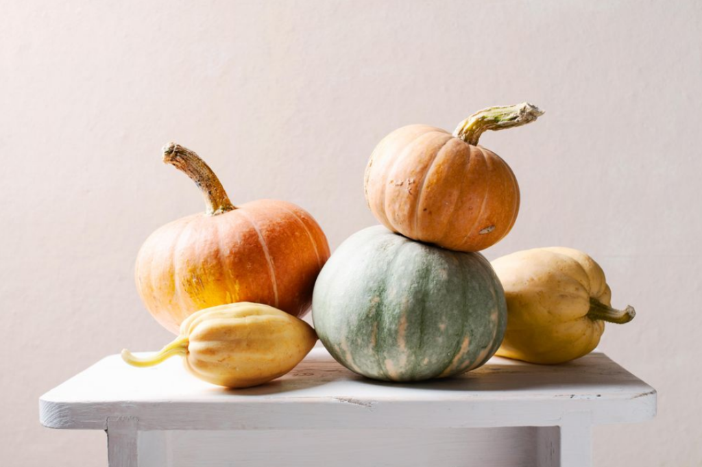 Soft neutral-toned lifestyle photo of a stack of several small, multi-colored pumpkins on a white table against a beige backdrop.