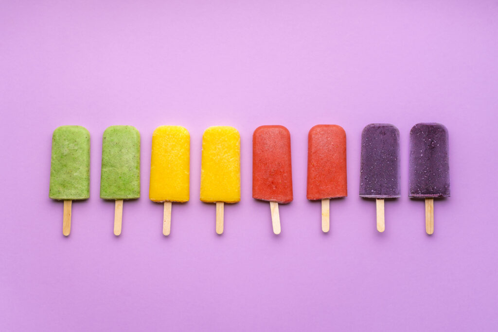 flay lay stock photo of colorful popsicles on bright purple backdrop 