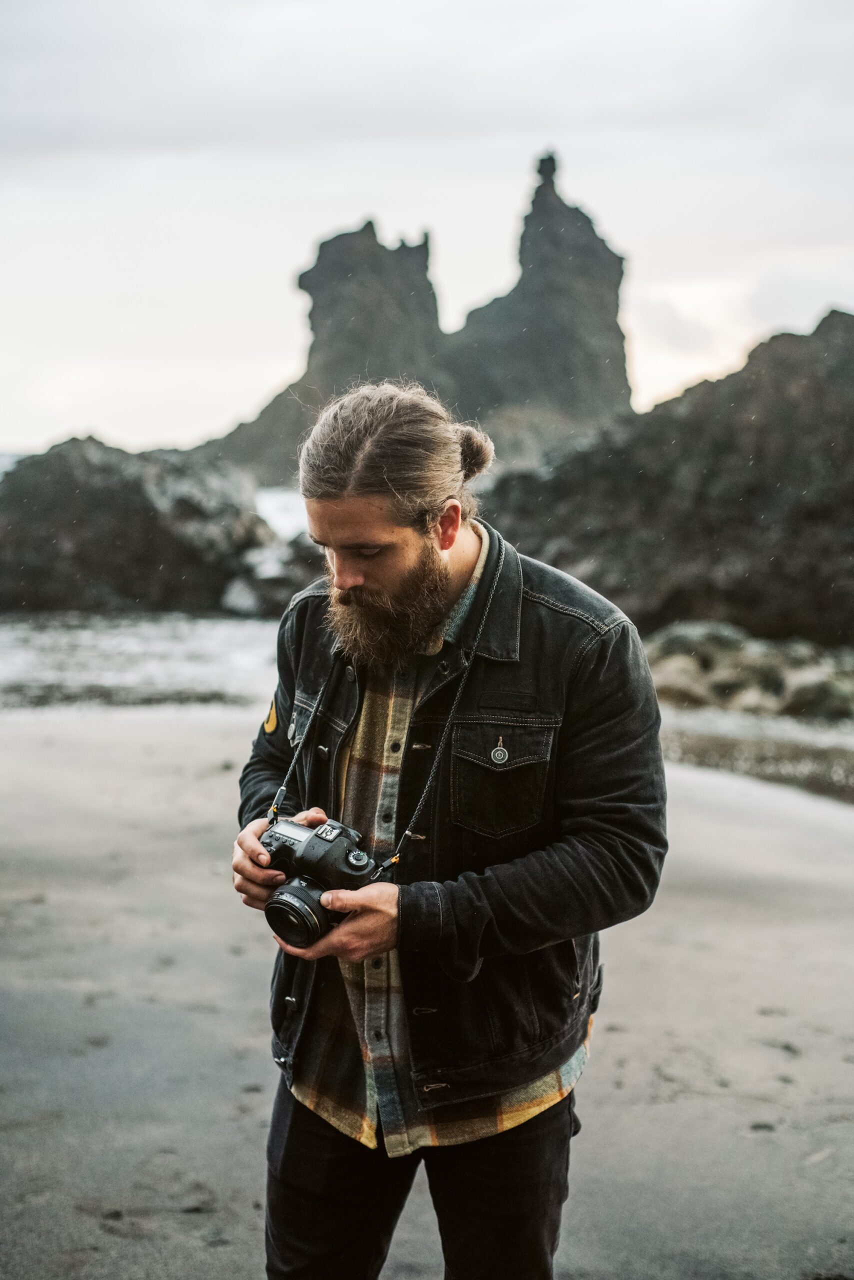 A man looks at his camera and thinks about how he will edit photos. He may use tools like VSCO to create a marketable photography style, earning him more freelance photography jobs.